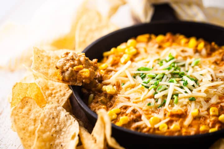 Corn dip with veggies and chorizo, scooped onto a tortilla chip.
