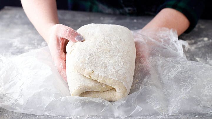 Homemade croissant dough, rolled and folded several times and being wrapped in plastic wrap.