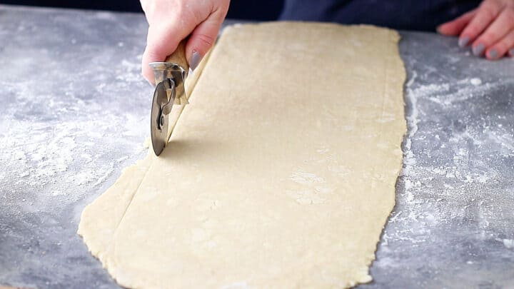 Trimming uneven edges off of croissant dough with a pizza cutter.
