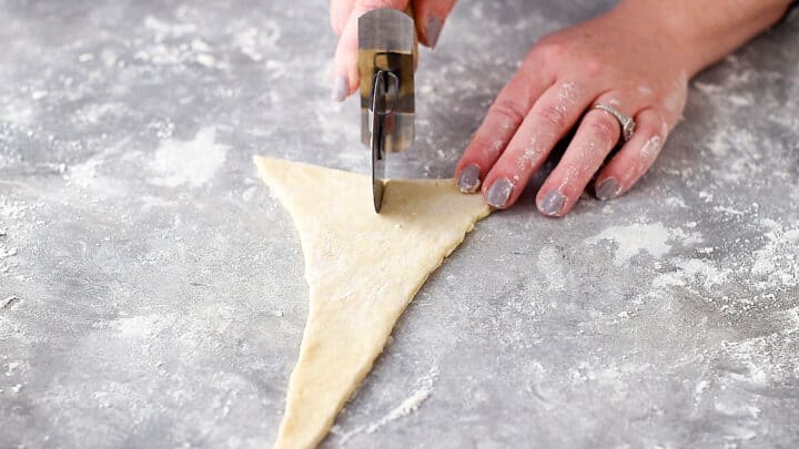 Cutting a notch into the wide end of a triangle of croissant dough.