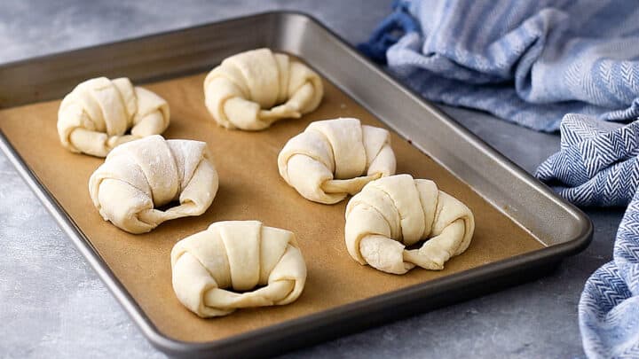 Unbaked croissants on a parchment-lined baking sheet.
