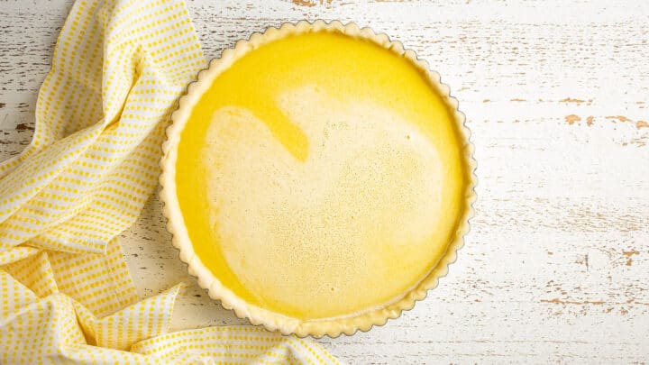 Immagine dall'alto di una crostata al limone non cotta, con un panno a quadretti giallo.