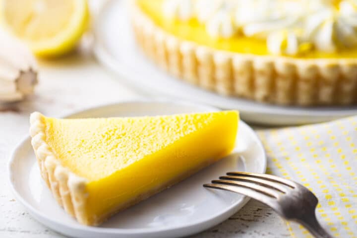 Slice of lemon tart with a fork and lemon reamer in the background.