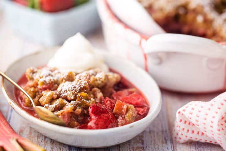 Recipe for strawberry rhubarb crisp, prepared and served in a small, shallow bowl and topped with whipped cream.