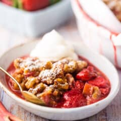 Strawberry rhubarb crisp served in a shallow bowl with whipped cream.