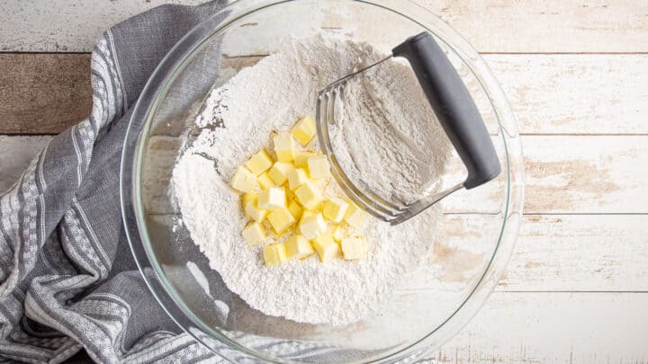 Butter added to dry ingredients, with a pastry blender tool.
