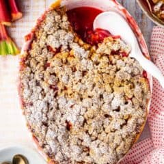 Overhead image of strawberry rhubarb crisp recipe, prepared and baked in an oval dish and surrounded with fresh strawberries and rhubarb stalks.