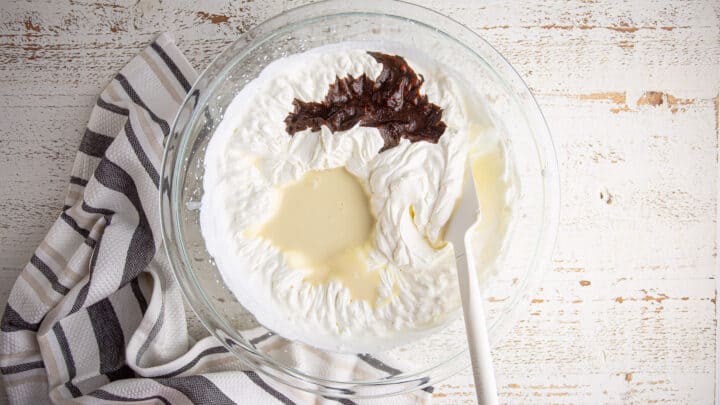 Adding condensed milk and instant espresso to a large bowl of whipped cream.