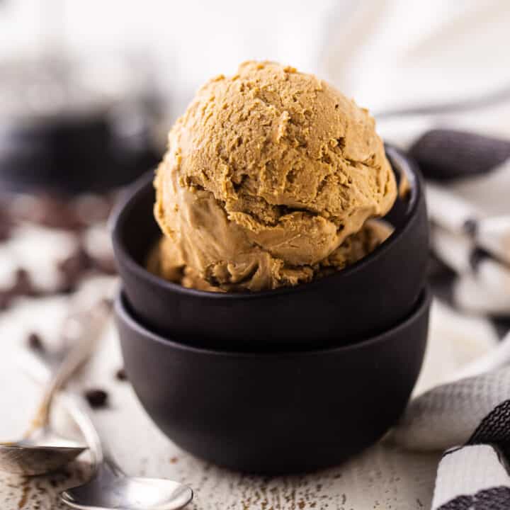 A scoop of coffee ice cream in a dark brown bowl, surrounded by coffee beans.