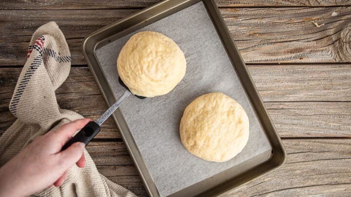 Draining boiled pretzel buns and placing them on a parchment-lined baking sheet.