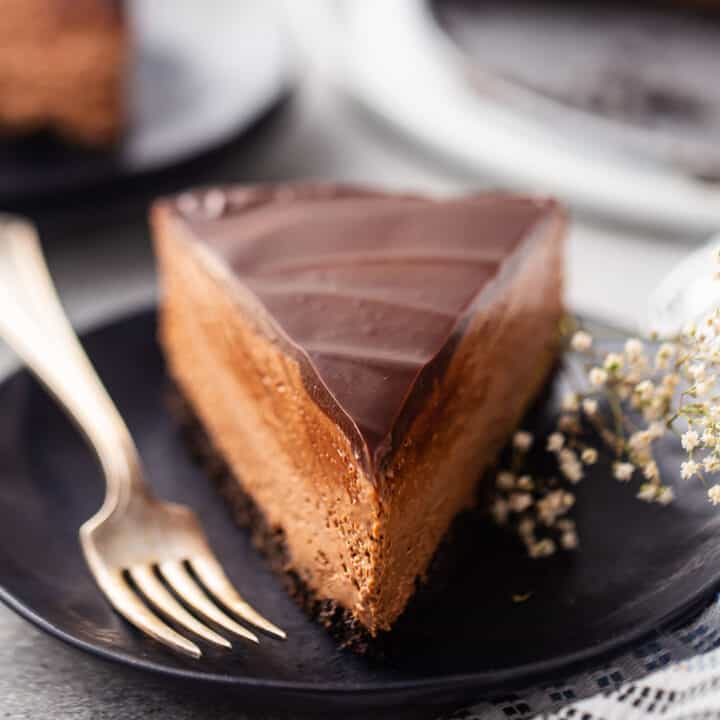 A slice of no-bake chocolate cheesecake on a dark plate with a vintage silver fork.
