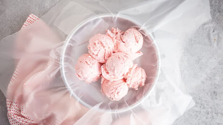 Scoops of strawberry ice cream in a plastic wrap lined cake pan.
