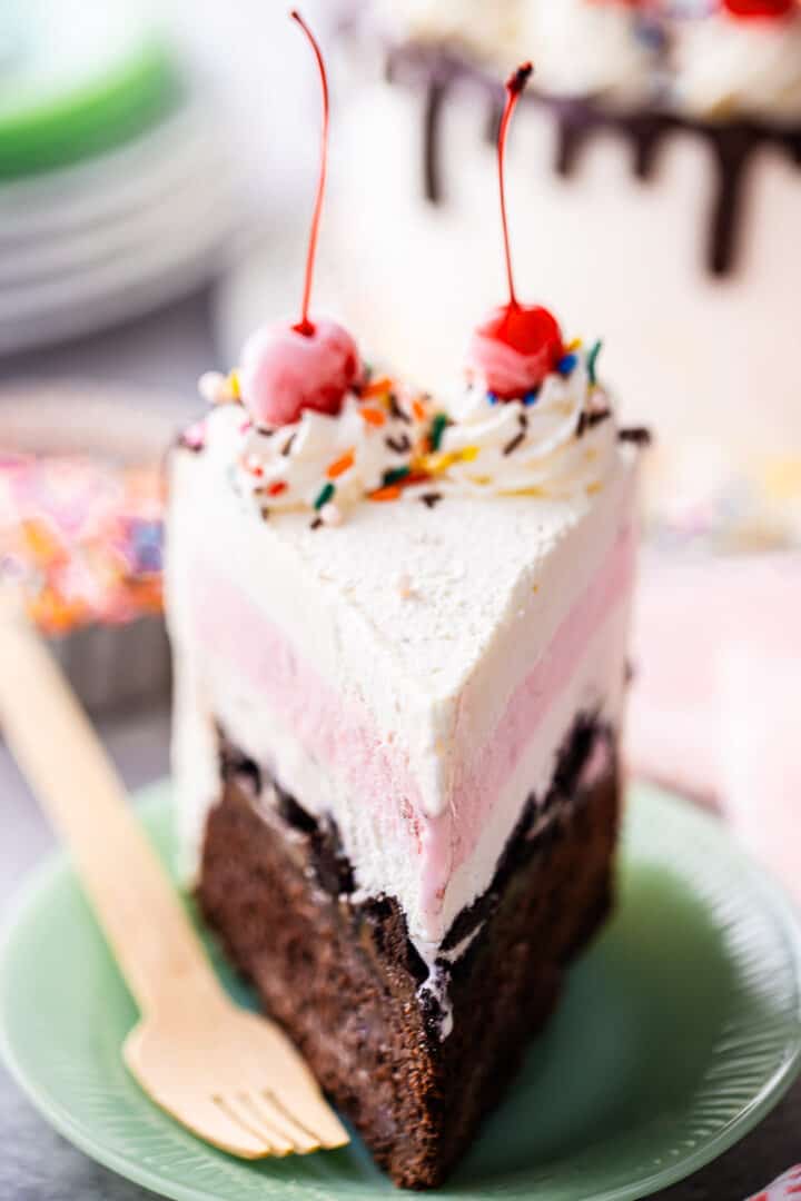 A tall slice of homemade ice cream cake, with rainbow sprinkles and a cherry on top.