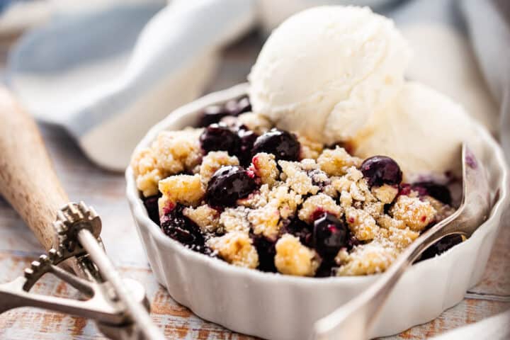 Blueberry crumble in an individual serving dish with a striped cloth in the background.