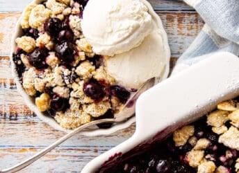 Blueberry crisp served in a shallow dish with a scoop of vanilla ice cream.