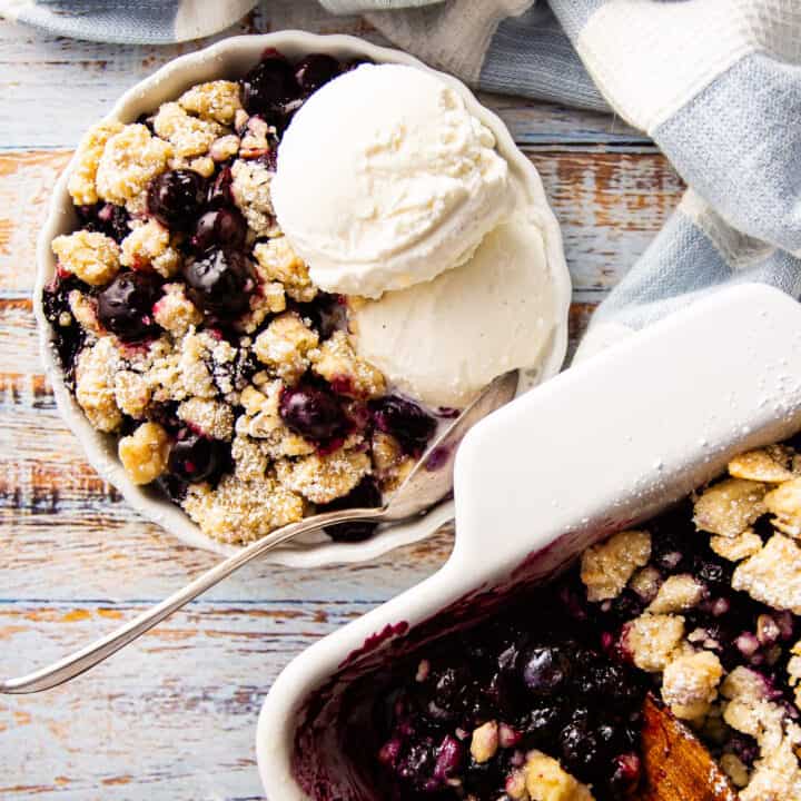 Blueberry crisp served in a shallow dish with a scoop of vanilla ice cream.