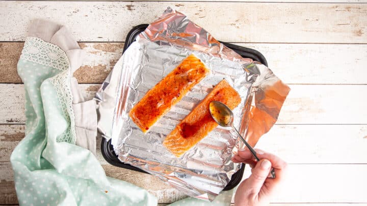 Spooning glaze onto seasoned salmon filets.
