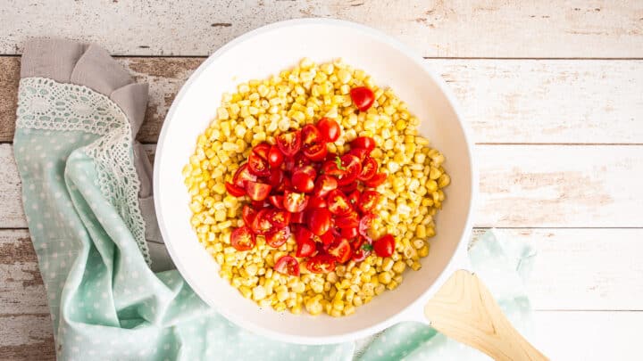 Sweet corn kernels in a white skillet with roughly chopped grape tomatoes.