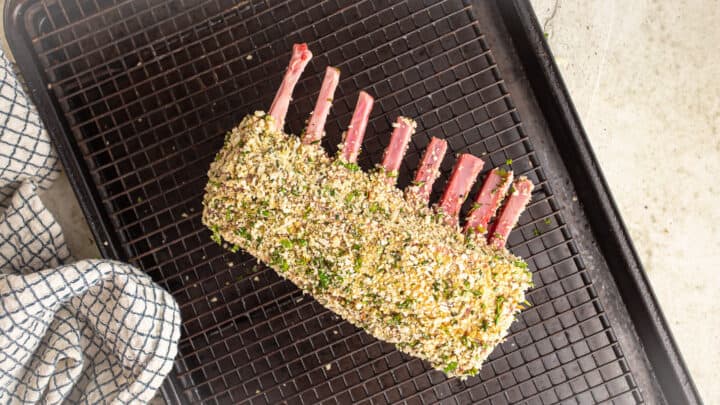 Herb encrusted rack of lamb on a wire rack.