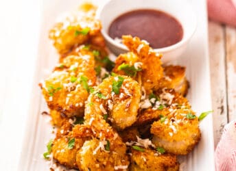 Coconut shrimp presented on a rectangular platter with dipping sauce.