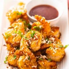 Coconut shrimp presented on a rectangular platter with dipping sauce.