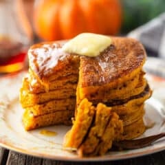 Pumpkin pancakes stacked on a vintage plate with butter and syrup.