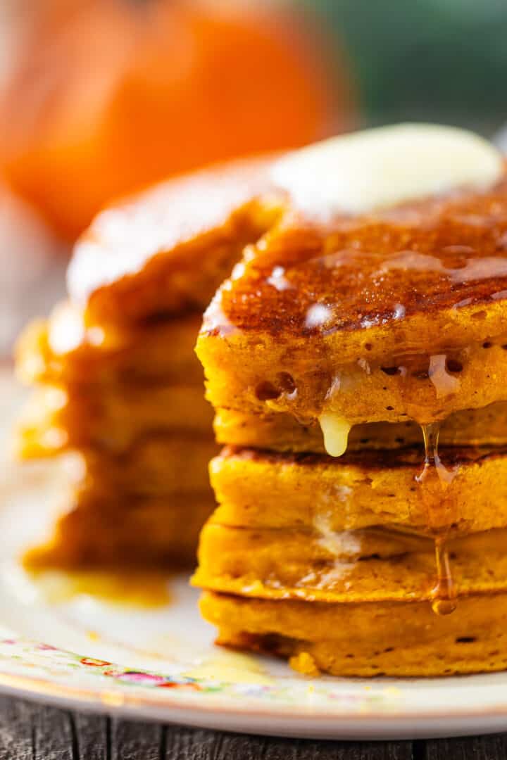 Pumpkin pancakes recipe, prepared, topped with melty butter, and drizzled with syrup.