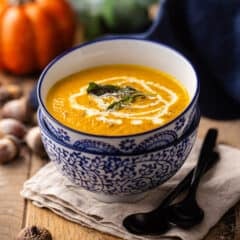 Pumpkin soup with sage and cream, served in a blue and white bowl.