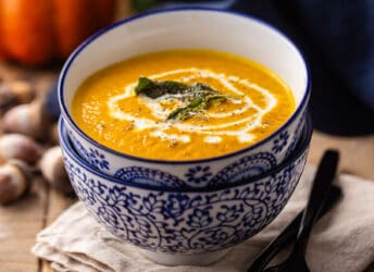 Pumpkin soup with sage and cream, served in a blue and white bowl.