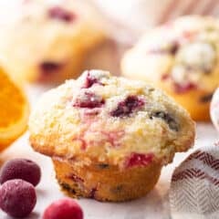Cranberry orange muffin displayed on a marble background with frozen cranberries.
