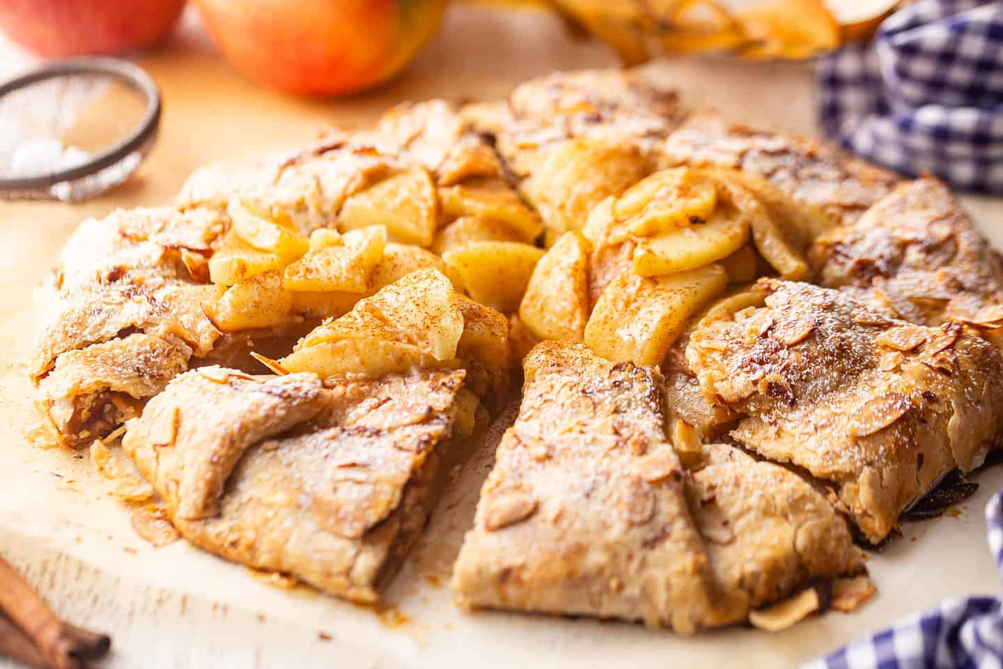 Recipe apple galette sliced and dusted with powdered sugar, with fresh apples in the background.