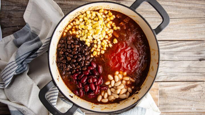 Adding tomatoes, beans, and corn to crockpot chili recipe.