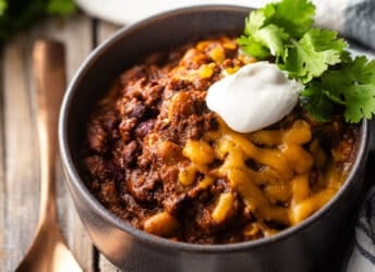 Best chili con carne recipe ever, served in a gray ceramic bowl with a copper spoon.