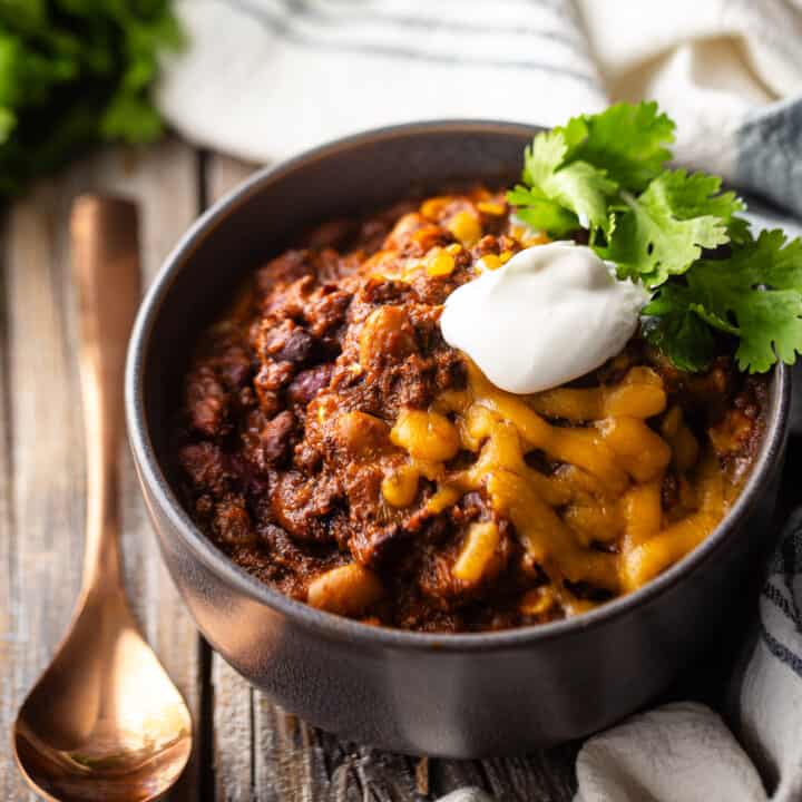 Best chili con carne recipe ever, served in a gray ceramic bowl with a copper spoon.