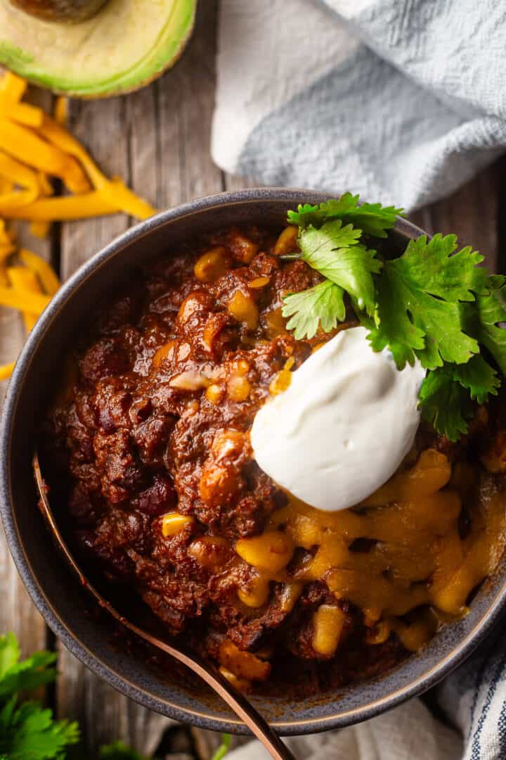 Beef chili recipe, prepared, cooked, and topped with cheese, sour cream, and fresh cilantro.