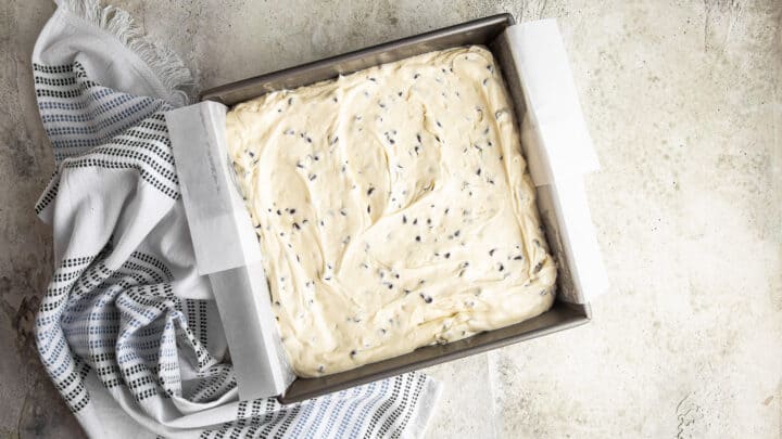 Chocolate chip cake batter smoothed to an even layer in a square baking pan.