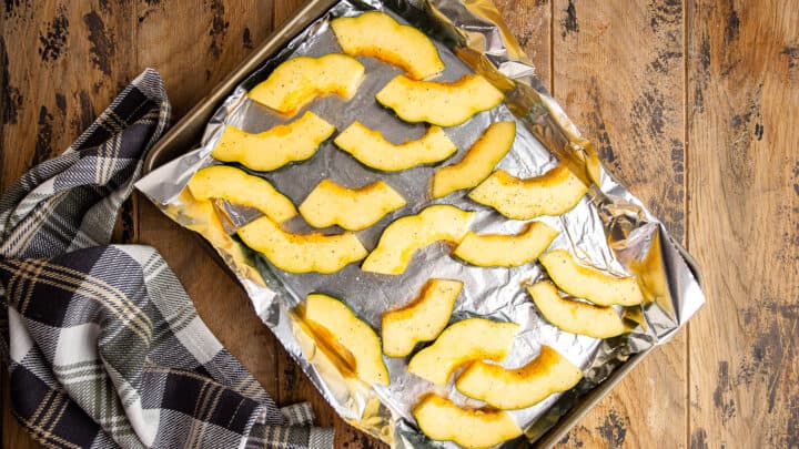 Slices of acorn squash seasoned and arranged in a single layer on a baking sheet.