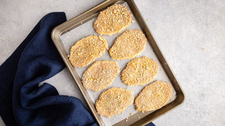 Breaded pork cutlets on a parchment-lined baking sheet.