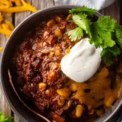Beef chili recipe, prepared, cooked, and topped with cheese, sour cream, and fresh cilantro.