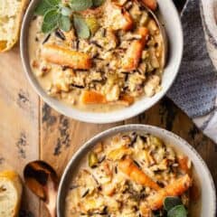 Two bowls of creamy chicken and wild rice soup served on a distressed wooden tabletop.
