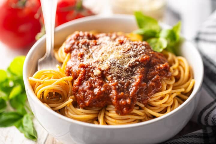 A white ceramic bowl filled with pasta and topped with tomato sauce.