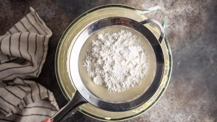 Sifting flour into whipped eggs and sugar, with a fine mesh sieve.