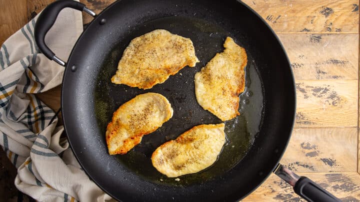 Seasoned, flour-dusted chicken cutlets sauteeing in olive oil.