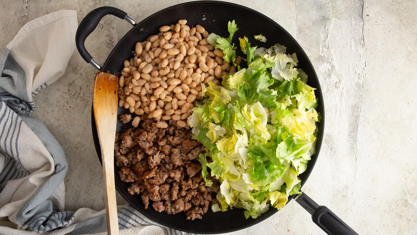 Crumbled sausage, escarole, and white beans in a large skillet.