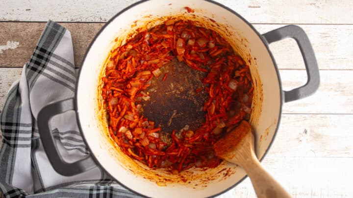 Browning tomato paste in a large pot with vegetables and seasonings.