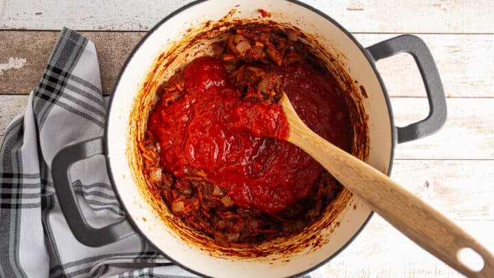 Adding crushed tomatoes to make tomato sauce.