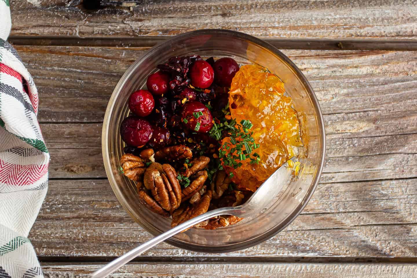 Cranberries, pecans, marmalade, rosemary, and crushed red pepper flakes, in a glass bowl.