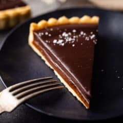 Chocolate caramel tart on a dark blue plate with a vintage silver fork.