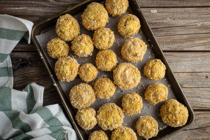 Breaded stuffed mushrooms on a parchment-lined baking sheet.