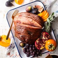Spiral sliced ham glazed with brown sugar and Dijon mustard and presented on a tray with seasonal fruits and herbs.